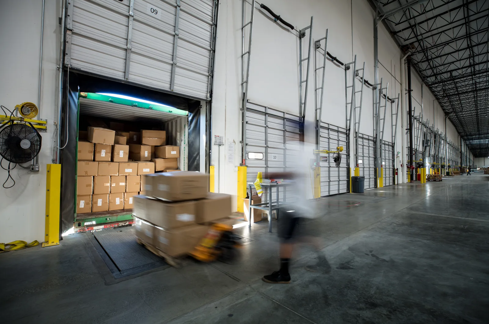 A worker with a hand truck moves freight across a warehouse loading dock.