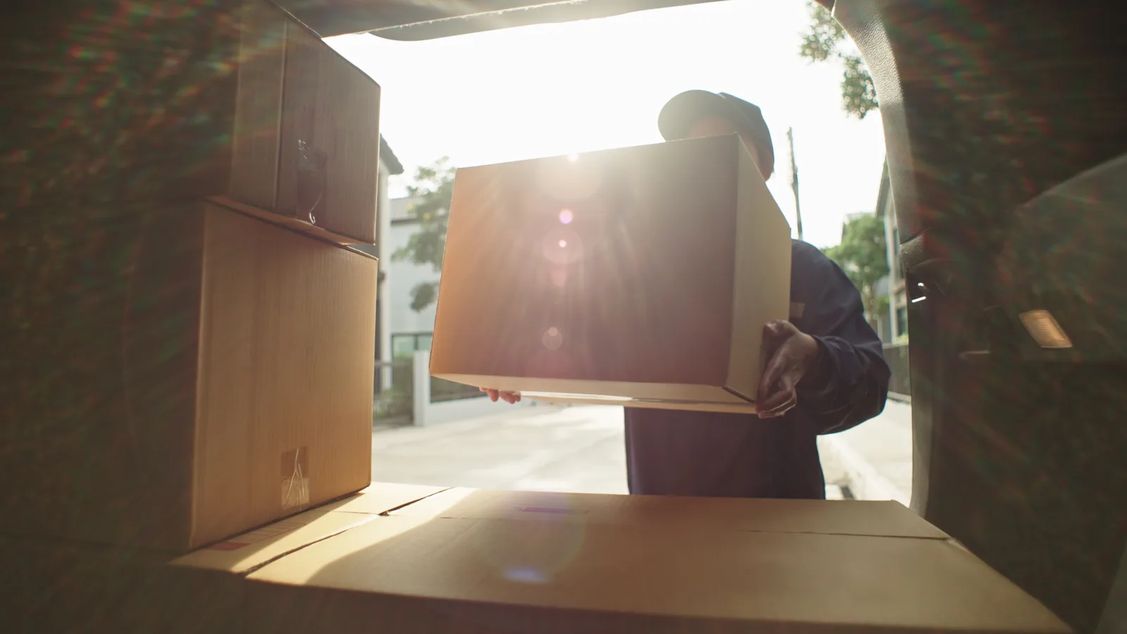 A courier pulls a package from the back of a van in low evening sun.